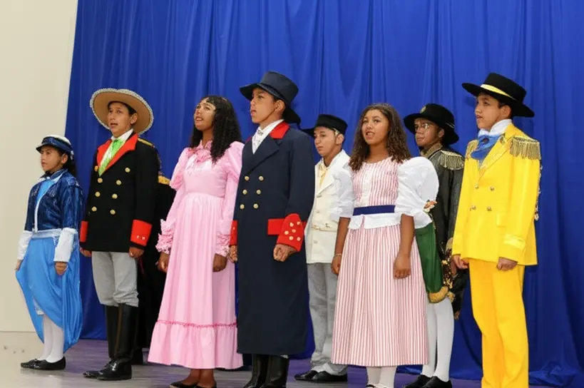Grupo de alunos em trajes de epoca encenando um momento da Proclamação da República em um palco escolar