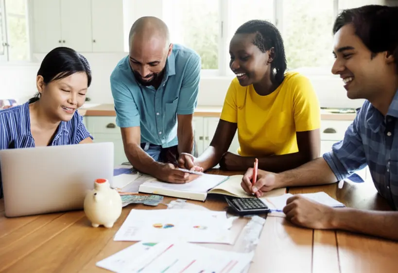 Pessoas diversas em uma mesa de cozinha discutindo um planejamento financeiro em um caderno e laptop