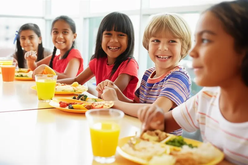 Crianças sorrindo e comendo refeições coloridas e nutritivas em um refeitório escolar de Sorocaba